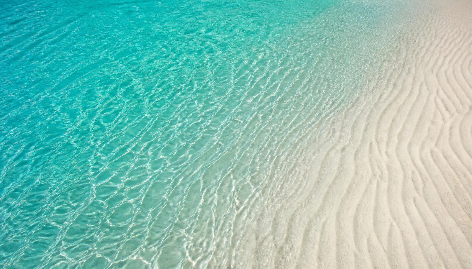 Aerial view of turquoise water meeting rippled pale sand