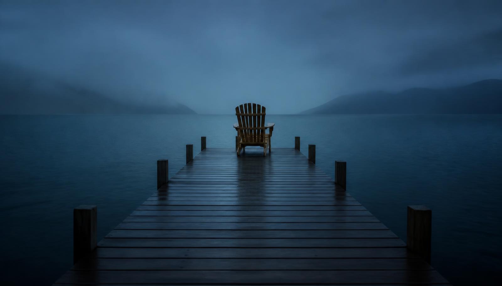 Empty wooden chair at the end of a quiet pier at blue hour above still dark water